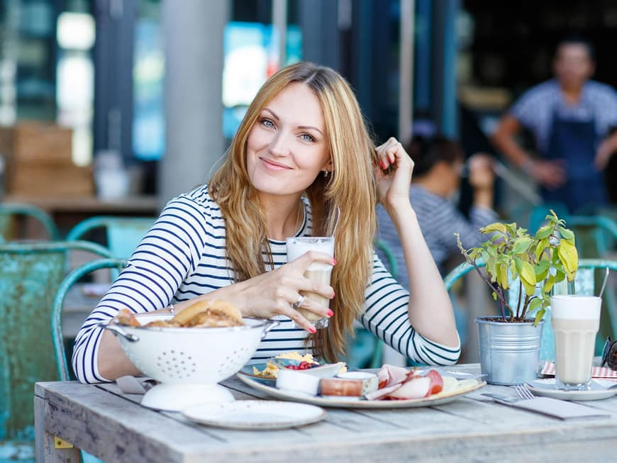 Frau sitzt draußen im Café mit Frühstück und Kaffee