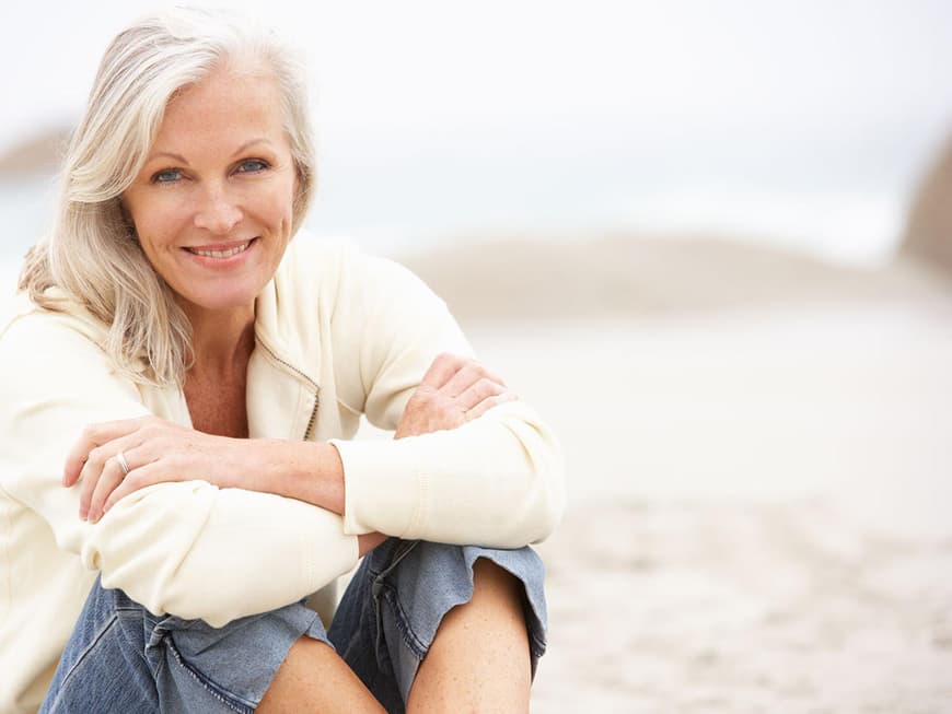 Frau mittleren Alters sitzt am Strand