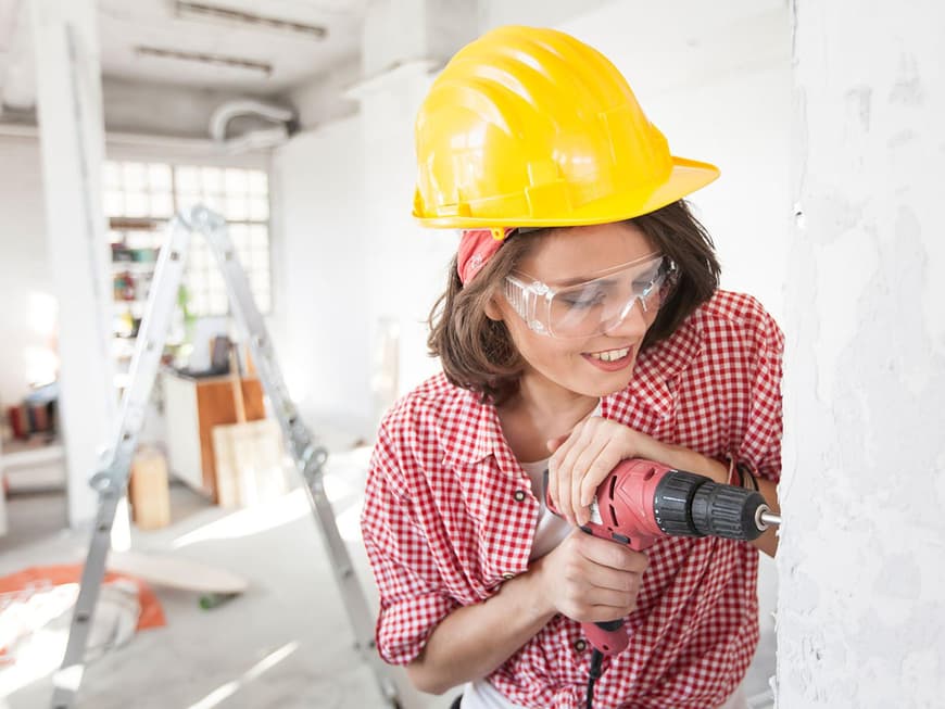 Frau mit Bauhelm bohrt in eine Wand