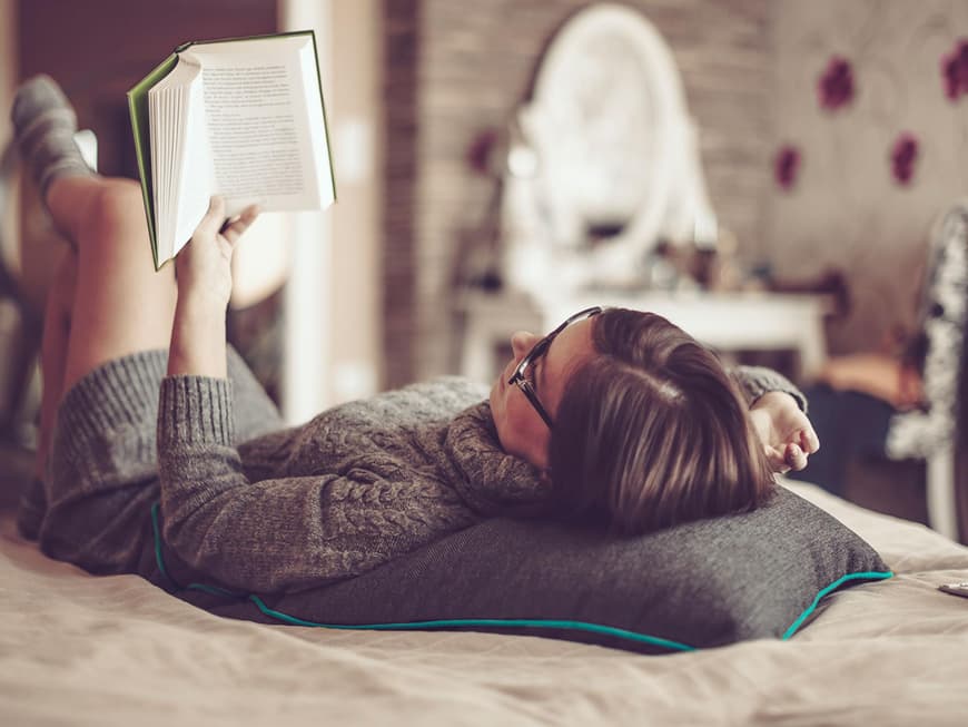 Frau liest mit Strickpullover und Socken Buch auf dem Bett