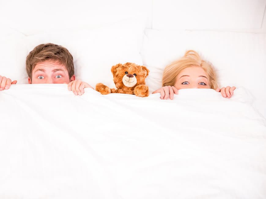 Paar unter der Decke im Bett mit Teddy in der Mitte