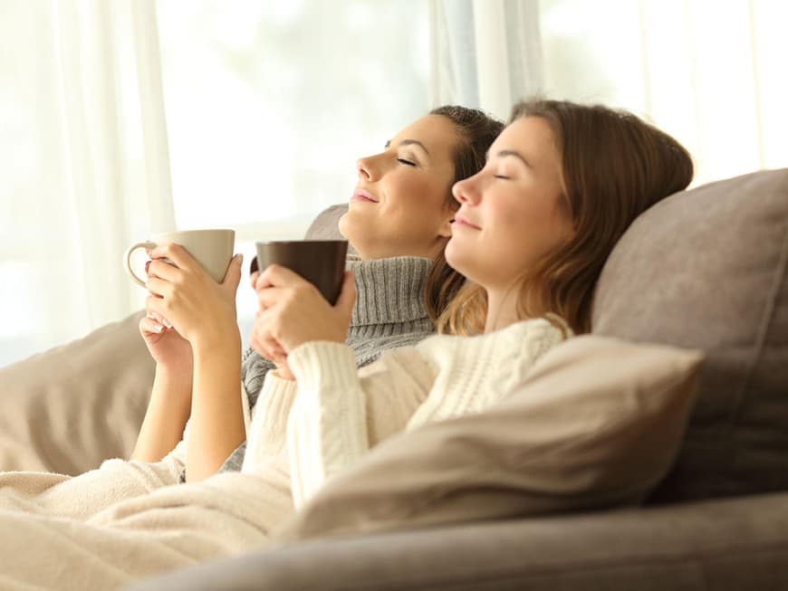 Zwei junge Frauen mit Decke und Tee auf dem Sofa