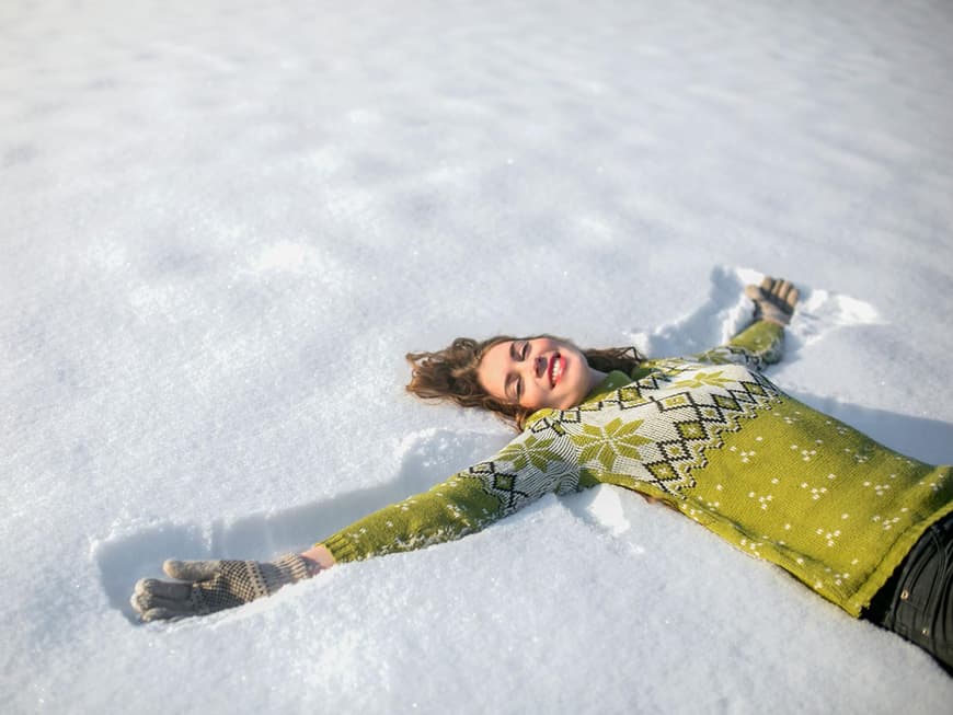 Junge Frau liegt mit Norwegerpullover und Handschuhen im Schnee