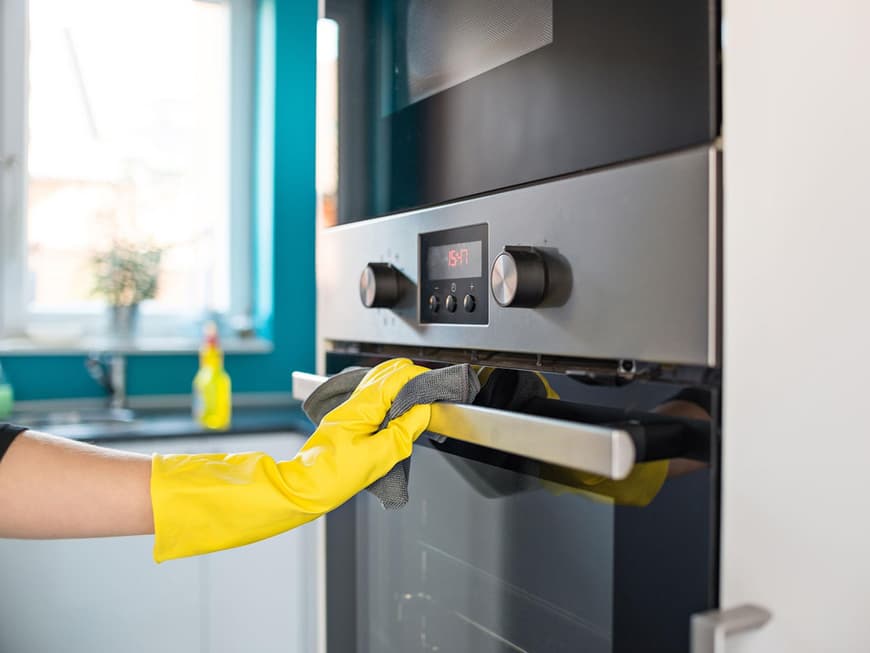 Ofen mit Gummihandschuhen und Lappen putzen