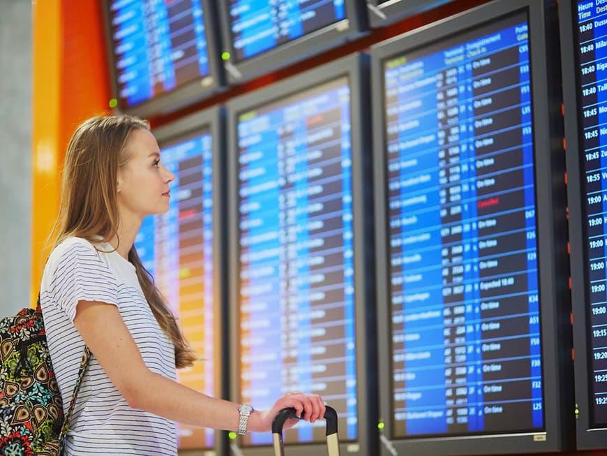 Junge Frau sieht sich Anzeigetafel am Flughafen an