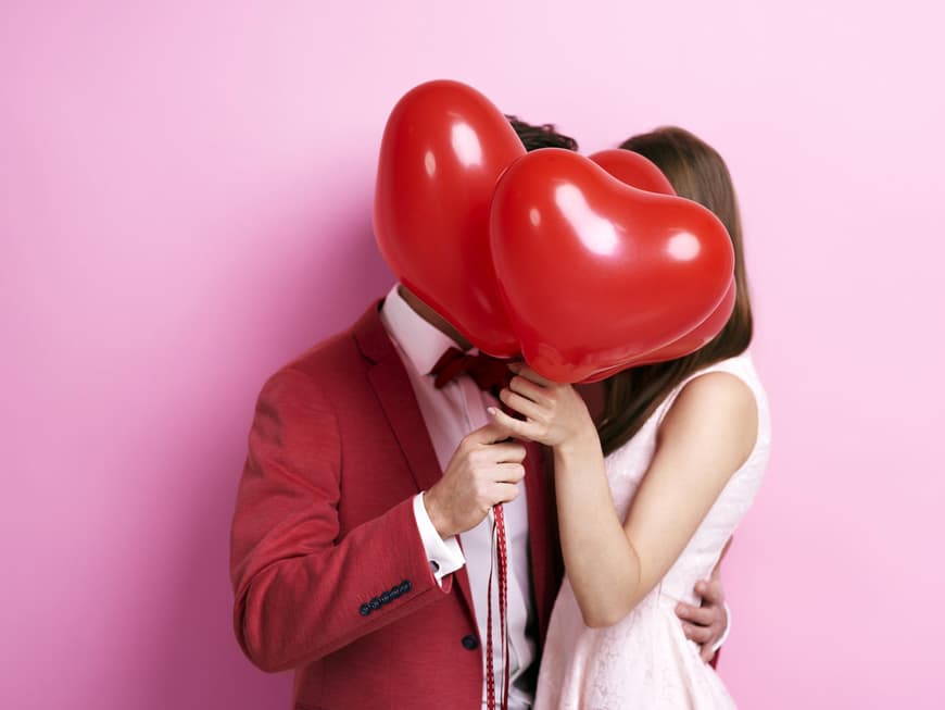 Paar küsst sich hinter Herzluftballons