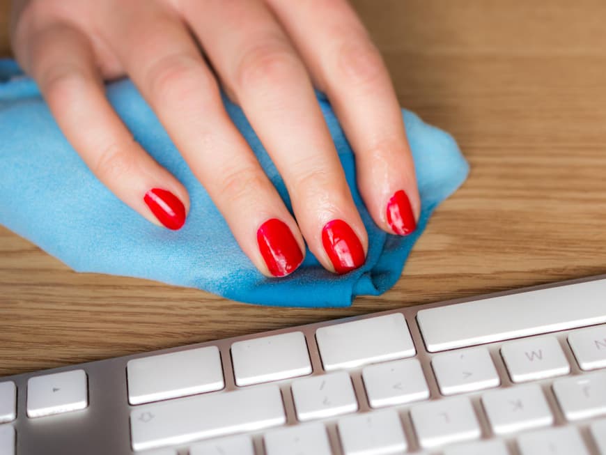 Damenhand mit rotem Nagellack reinigt Tastatur