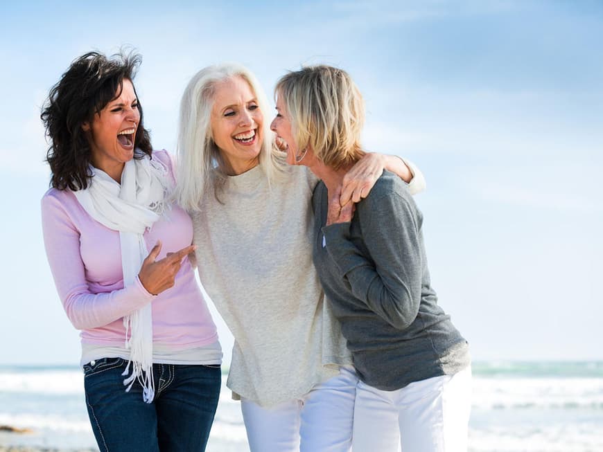 Drei Freundinnen Arm in Arm lachen am Strand