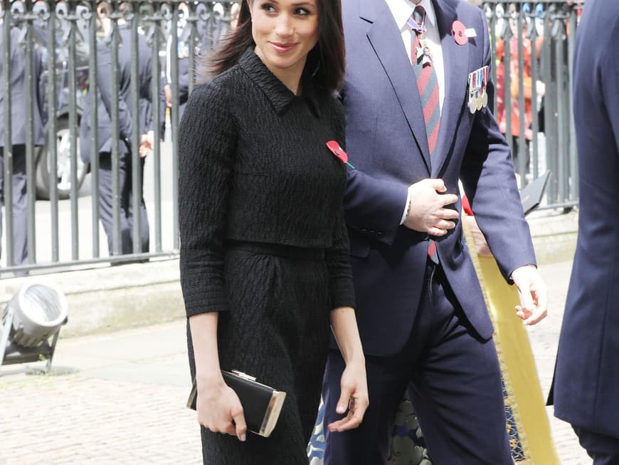Meghan Markle im eleganten, schwarzen Kostüm mit Bleistiftrock, kurzem Jäckchen, Barett und Highheels