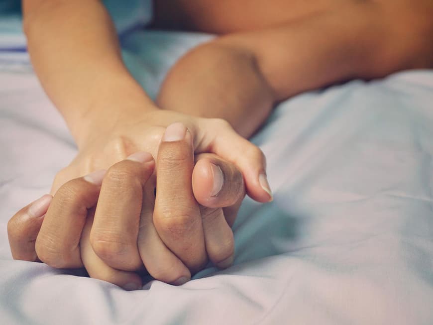 Hände berühren sich im Bett