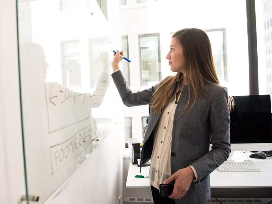 Frau im Blazer steht an einem Whiteboard