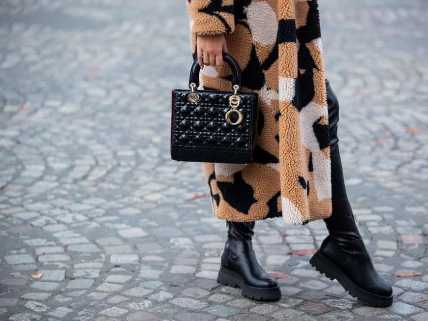 Stylish mit Fake-Fur-Mantel, schwarzen Stiefeln und Handtasche